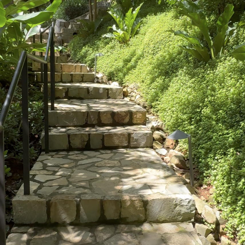 Stone pathway surrounded by tropical greenery leading up through a lush hillside resort garden, representing sustainable luxury travel.