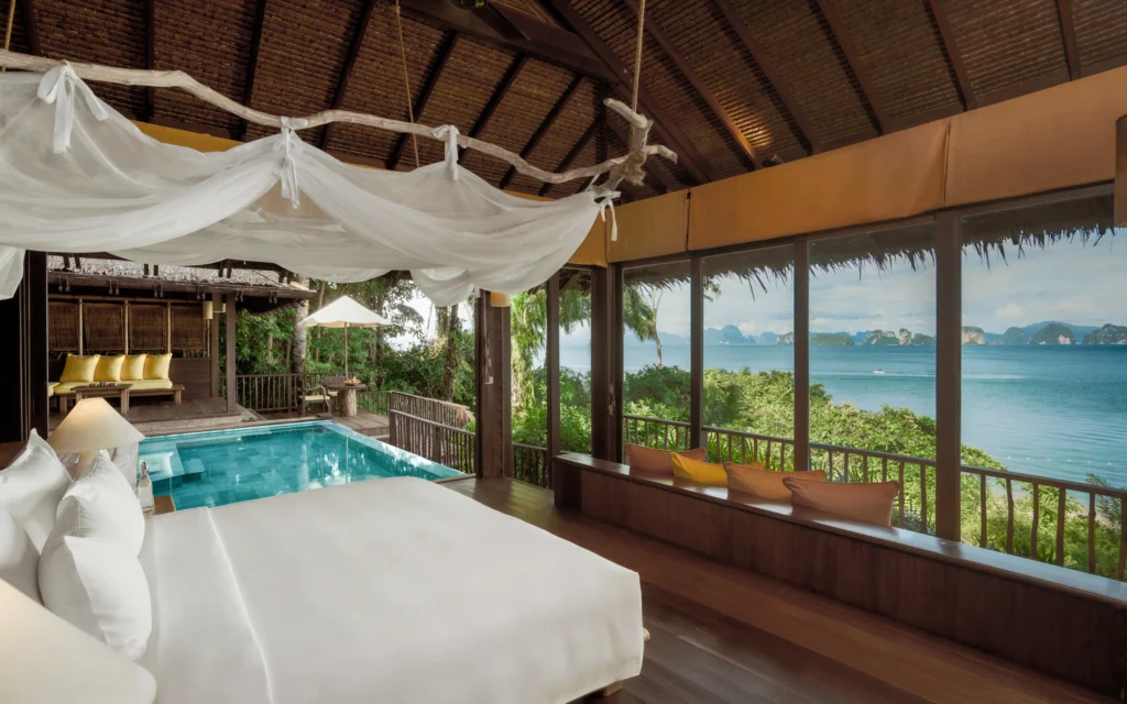 Luxury overwater villa bedroom at Six Senses Yao Noi in Thailand with canopy bed, private plunge pool, and panoramic views of Phang Nga Bay.