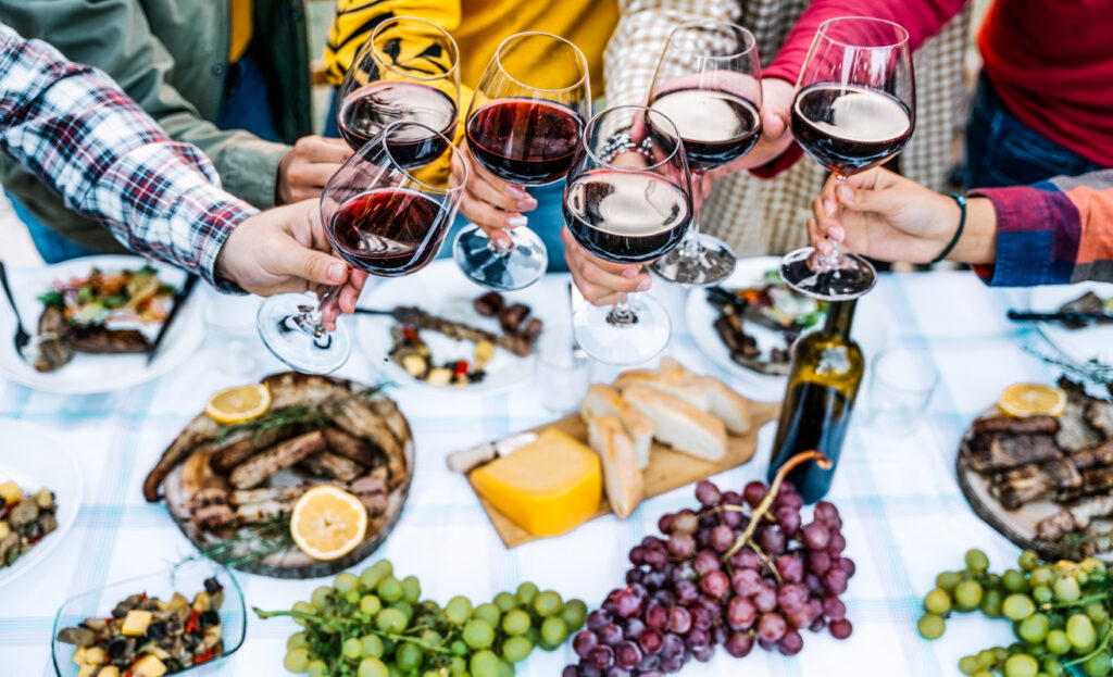 Group of young people hands toasting red wine glass at winery party - Multiracial friends celebrating at bbq dinner at home garden - Harvest time outside at farm house vineyard countryside