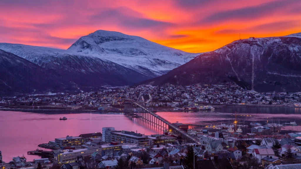 Pink and orange sunset over snowy mountains and a harbor city with a long bridge in Arctic Norway